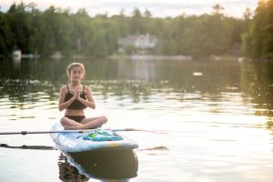 Health benefits of lakefront living: Woman meditating on paddle board