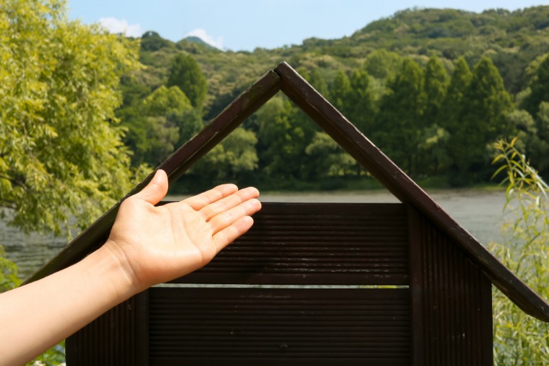 Hand Presenting Wooden House Beside A River